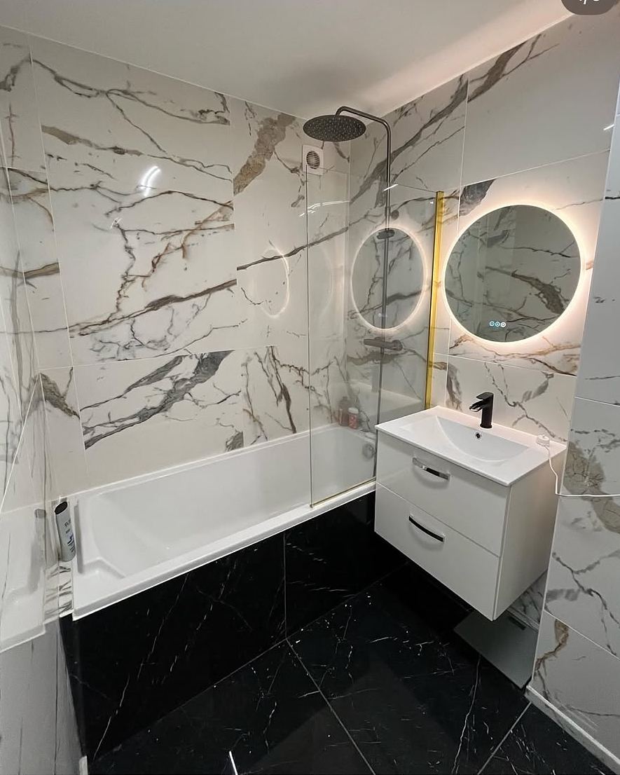 Après travaux : même salle de bain en grès cérame effet marbre, sol en marbre noir, meuble suspendu et miroir rond rétroéclairé.
