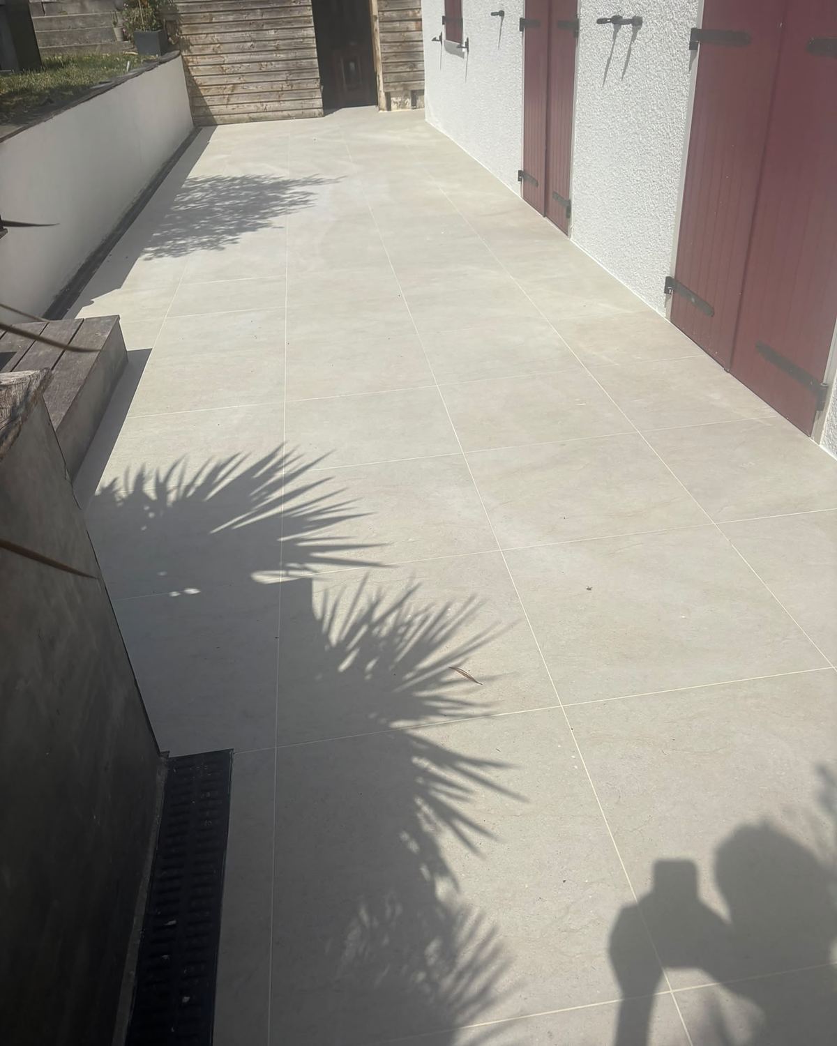 Après travaux : même terrasse refaite en grès cérame beige grand format, avec un caniveau le long de la façade.