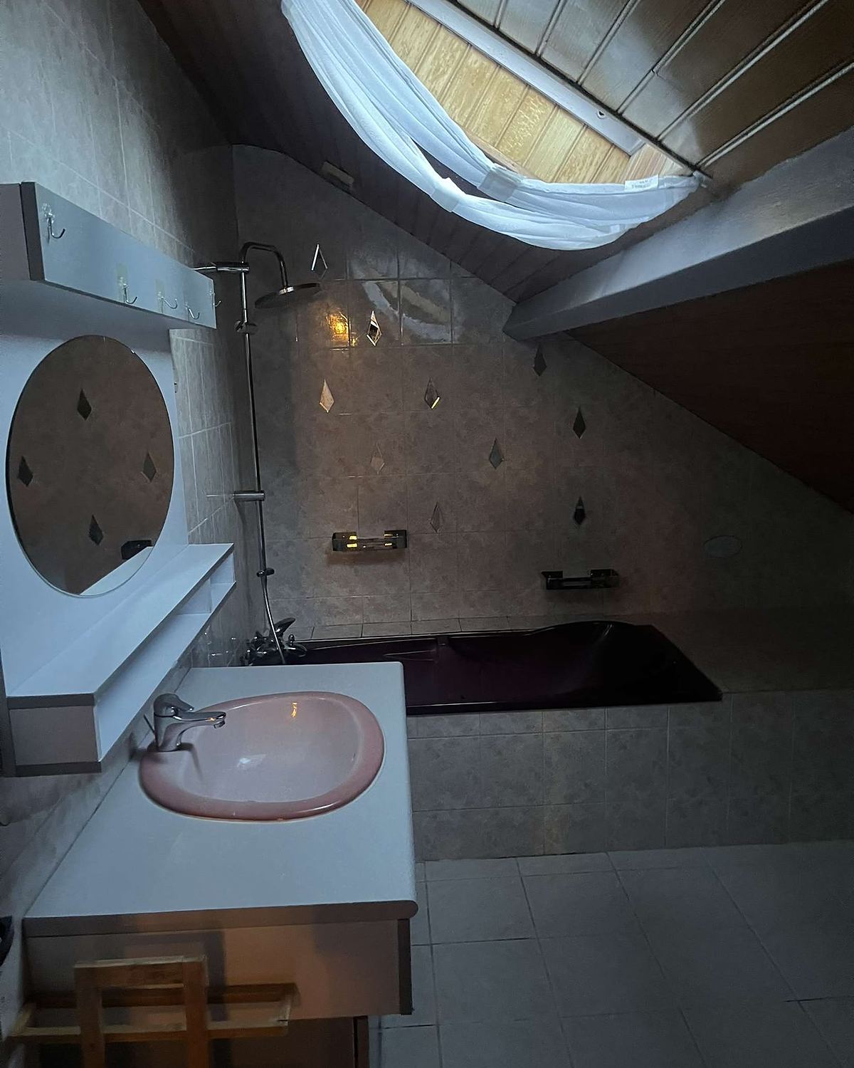 Avant travaux : salle de bain sous combles avec carrelage brun, vasque rose et baignoire foncée.
