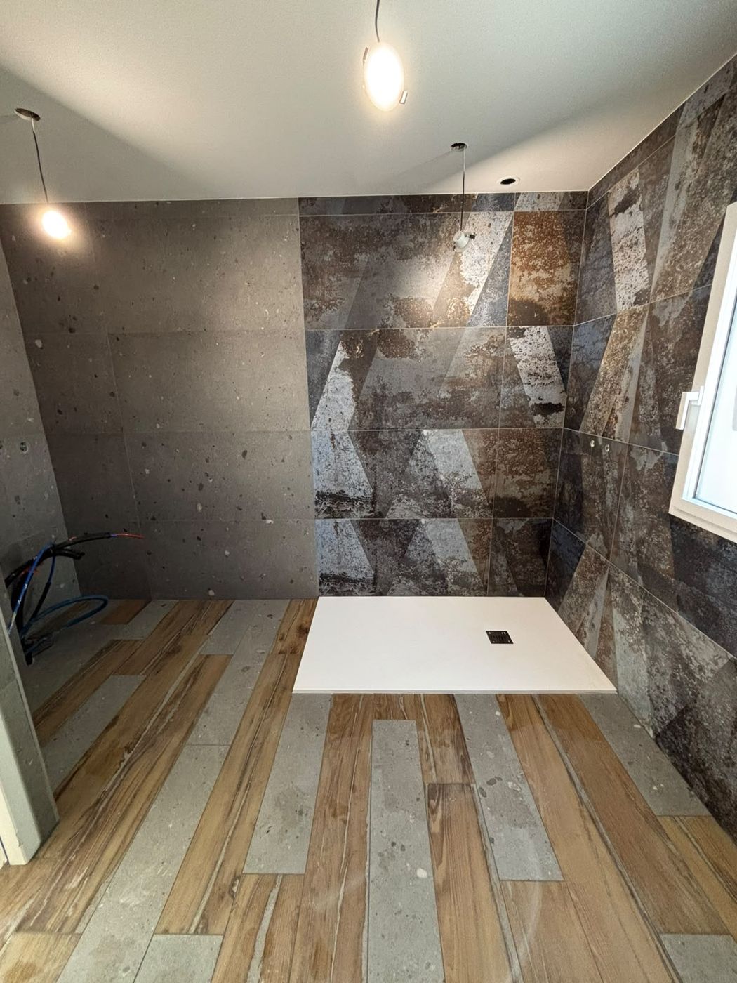 Salle de bain avec un mur en grès cérame effet métal oxydé, un mur béton, un sol imitation bois et un receveur de douche blanc.