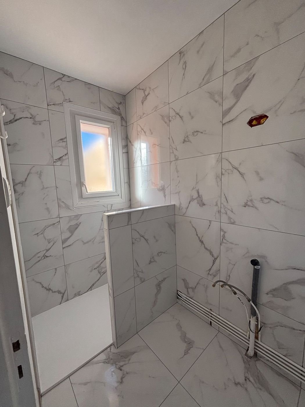 Salle de bain entièrement carrelée en grand format effet marbre blanc, avec un muret de douche carrelé.