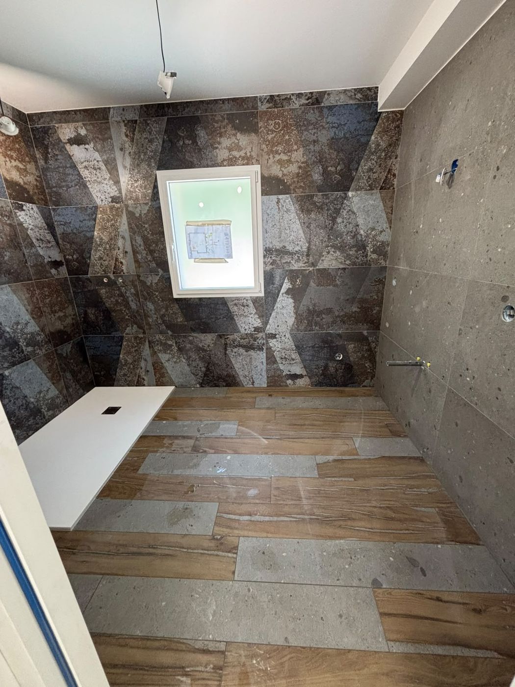 Douche à l'italienne sans marche, mur en carrelage effet métal et sol imitation bois.