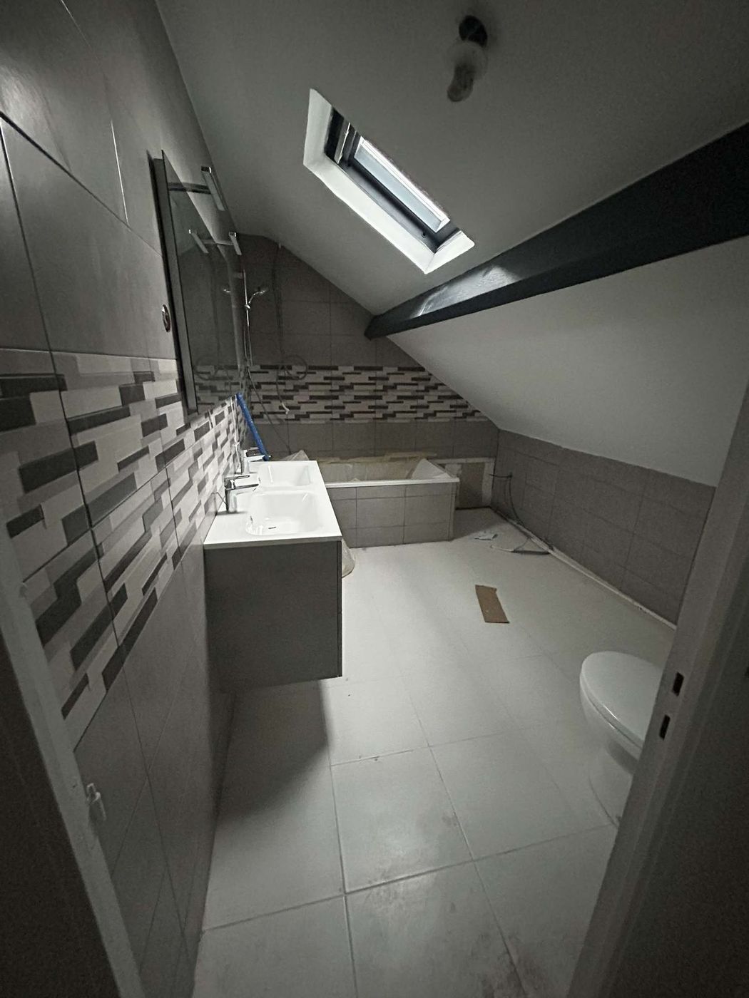 Salle de bain aménagée sous les rampants du toit, avec une frise en mosaïque et un plan vasque suspendu.