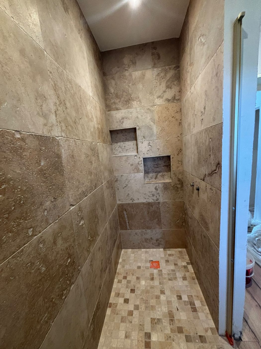 Douche à l'italienne en travertin avec niche encastrée et receveur carrelé en petite mosaïque.