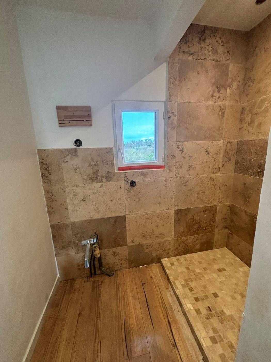 Salle d'eau avec murs en travertin sur la moitié de leur hauteur, sol imitation parquet et receveur en mosaïque.