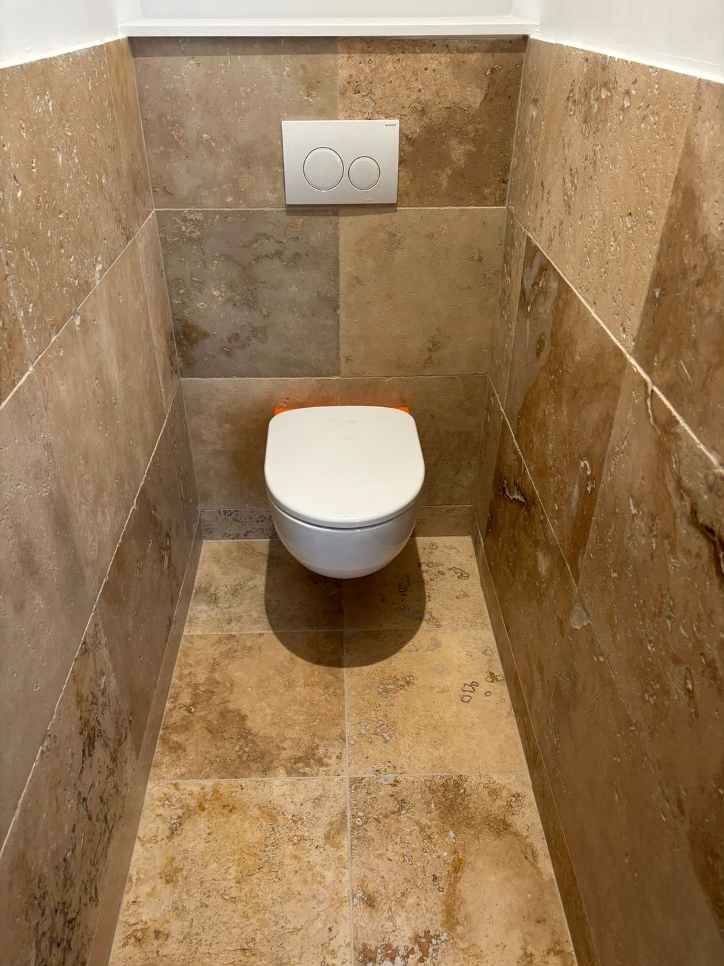 Toilettes suspendues avec coffrage carrelé, murs et sol entièrement en travertin.