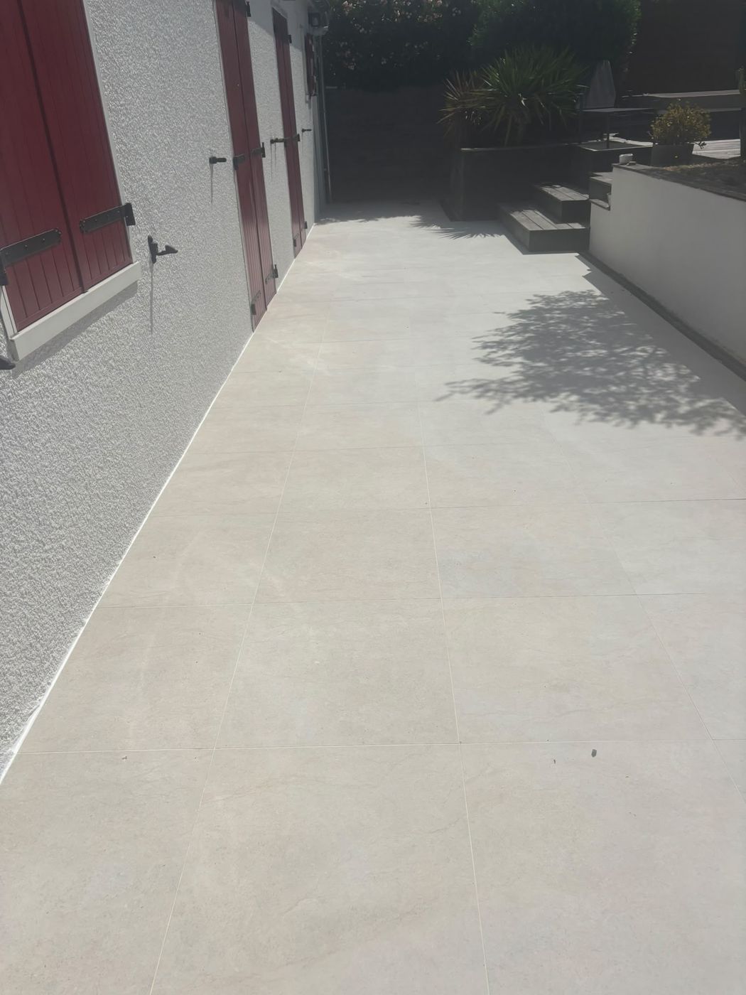 Terrasse extérieure carrelée en grès cérame beige grand format, le long de la façade d'une maison.